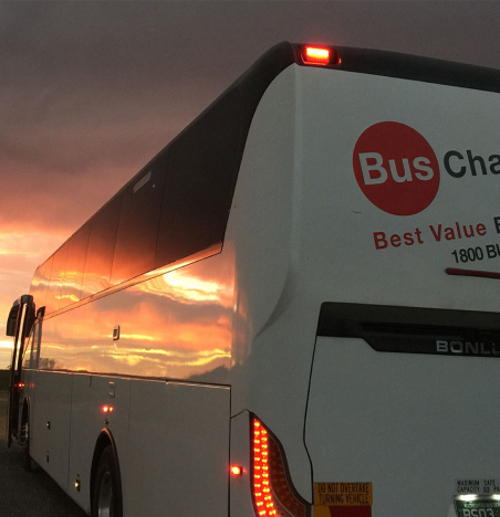 Bus charter airport transfer driving at dusk with sunset reflecting in mirrors