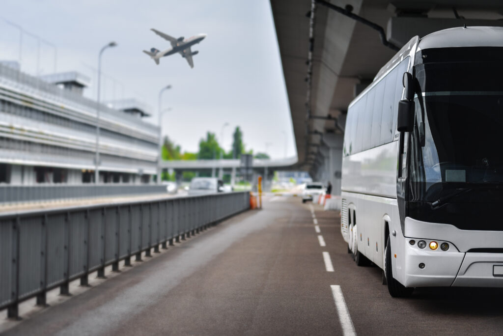 Airport transfer bus leaving airport with guests, airplanes flying in background.